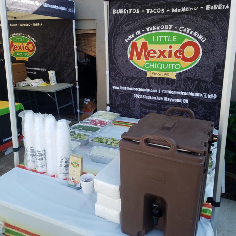 Little Mexico Chiquito catering setup with food trays, cups, and a large beverage dispenser.
