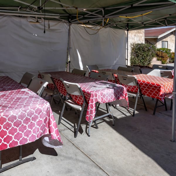 Outdoor dining area with tables covered in red and pink patterned tablecloths under a tent.