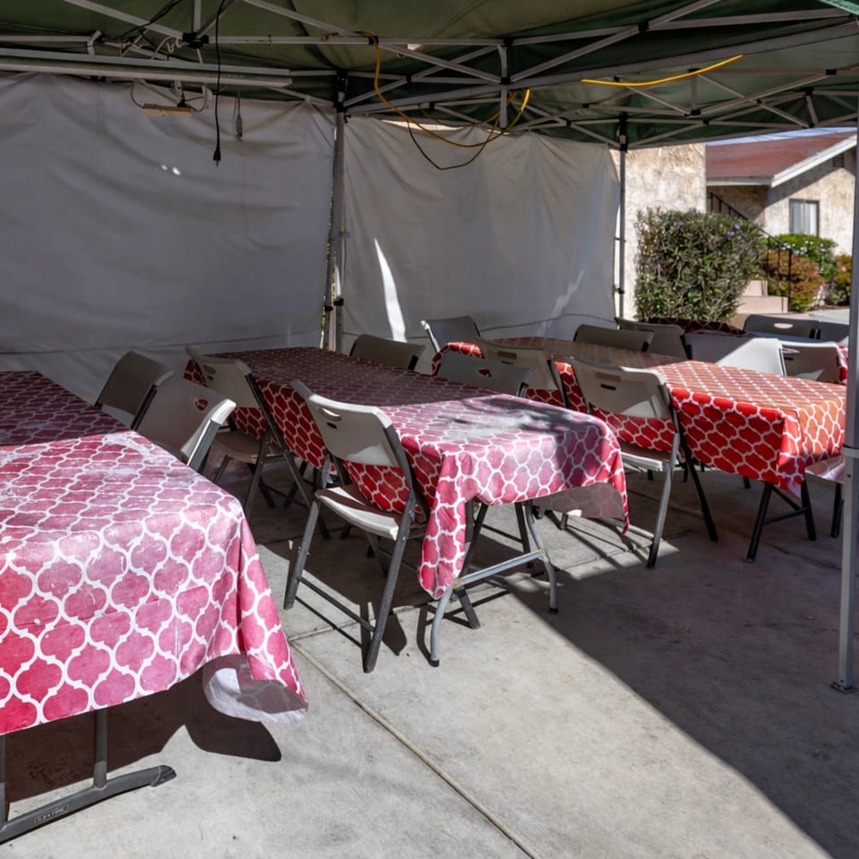 Outdoor dining area with tables covered in red and pink patterned tablecloths under a tent.