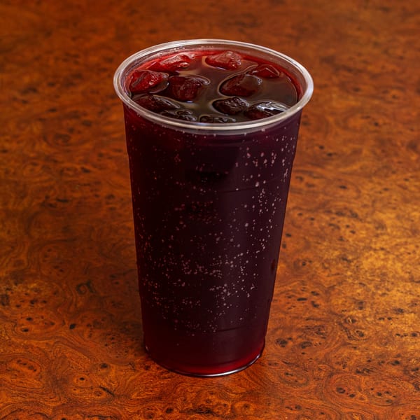 A plastic cup of dark red agua fresca with ice sits on a wooden table.