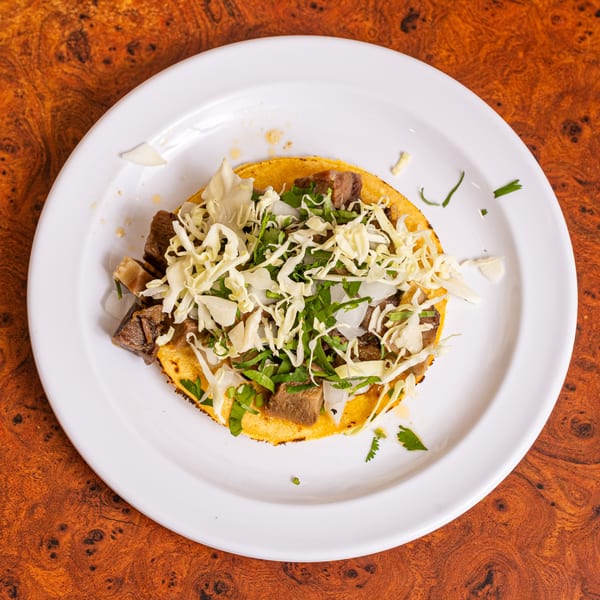 A Little Mexico Chiquito Mexican taco with meat, shredded cabbage, and cilantro on a white plate.