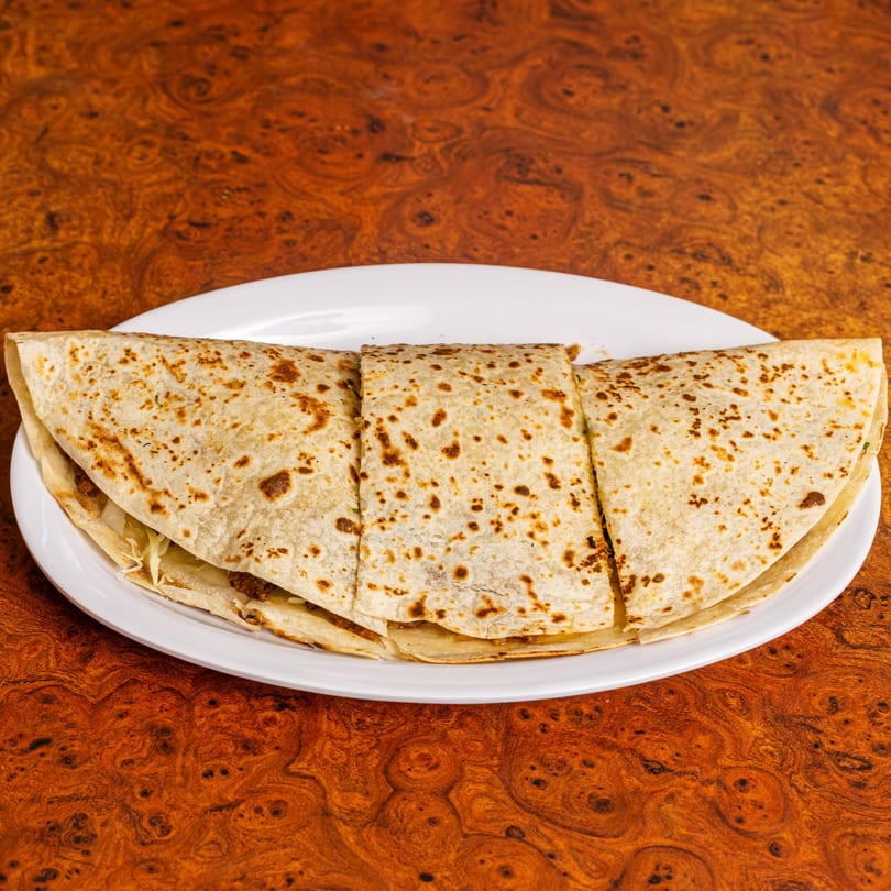 Three large, folded quesadillas with browned tortillas and filling, served on a white plate.