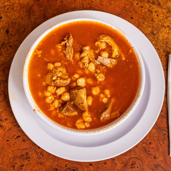 Close-up of a bowl of Little Mexico Chiquito's pozole, a rich red Mexican soup with meat and hominy.