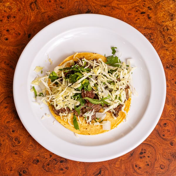 A Little Mexico Chiquito taco with shredded meat, cabbage, and cilantro on a white plate.