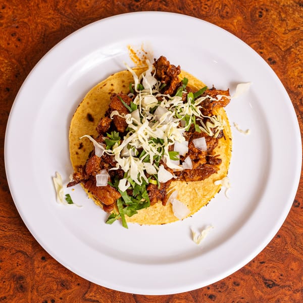 A single Mexican taco with seasoned meat, shredded cabbage, and cilantro on a white plate.