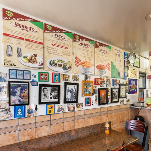 Restaurant interior with menu boards, framed photos, and a tiled counter with an orange soda bottle.