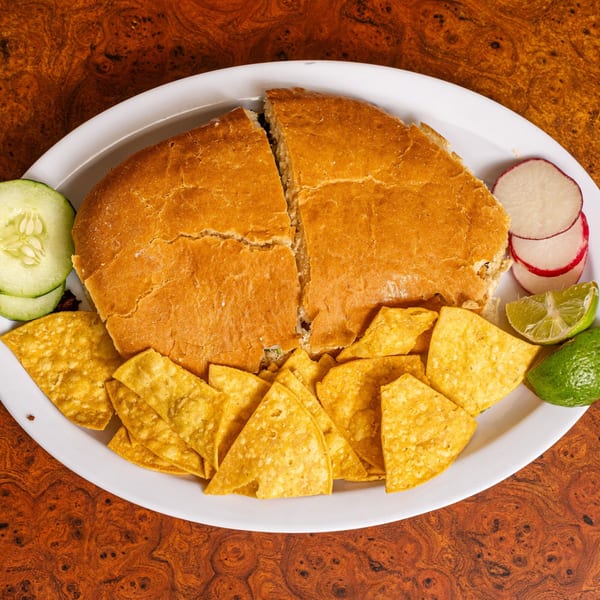 Mexican torta cut in half, served with tortilla chips, cucumber, radishes, and lime wedges.