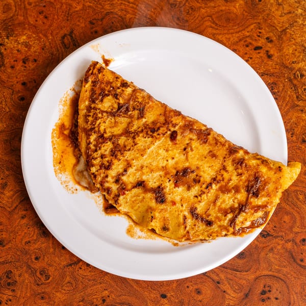A large, golden-brown Mexican quesadilla, drizzled with a rich red sauce, on a white plate.