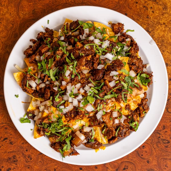 Mexican nachos with seasoned meat, diced onions, and cilantro on a white plate.