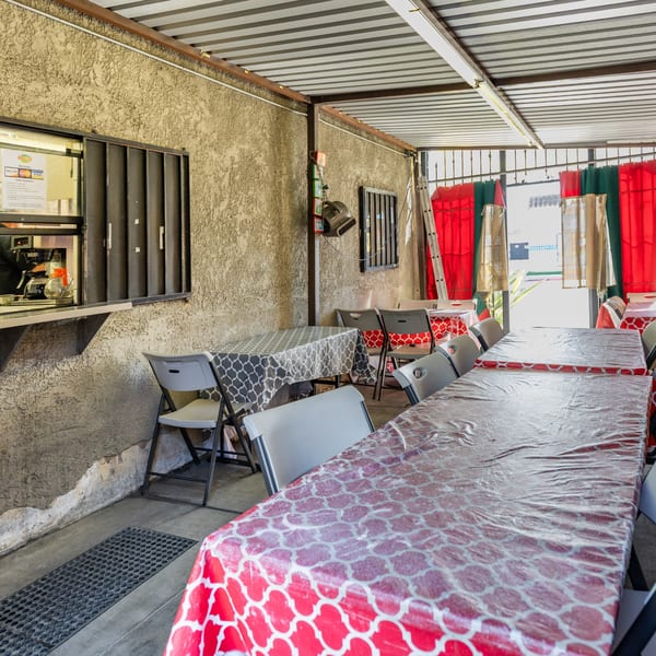 Outdoor patio dining area at Little Mexico Chiquito with patterned tablecloths, folding chairs, and a service window.