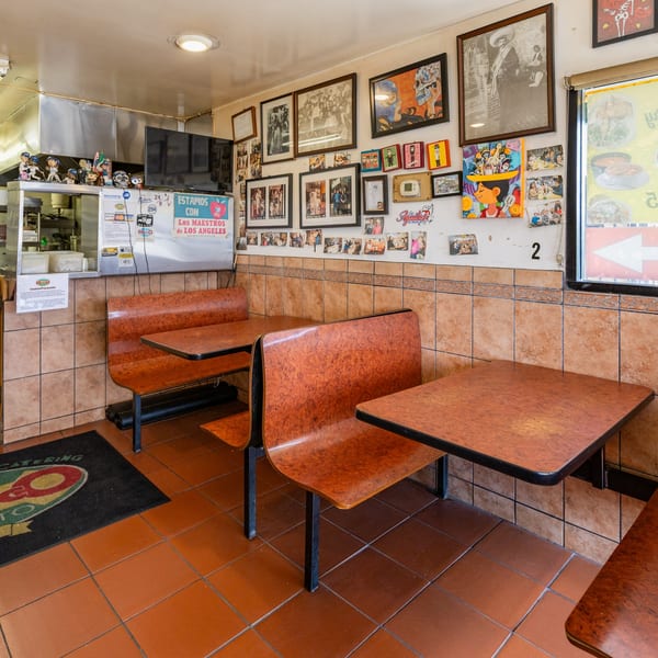 Interior of Little Mexico Chiquito with orange booths, tiled walls, and framed pictures on the wall.