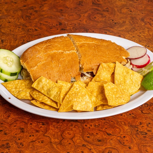 Mexican torta sandwich cut in half, served with tortilla chips, cucumber, radish, and lime.