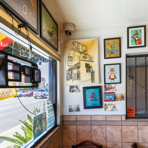 A corner of Little Mexico Chiquito restaurant with a window view of the street and framed art on the wall.