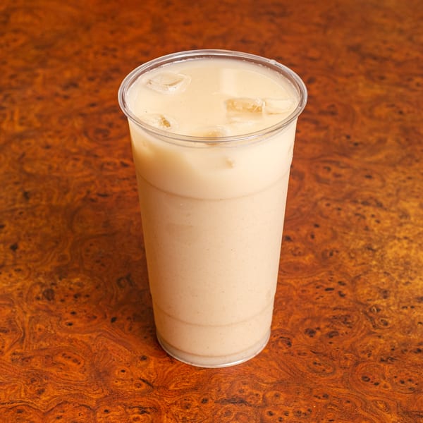 Horchata, a traditional Mexican rice drink with ice, in a clear plastic cup on a wooden table.