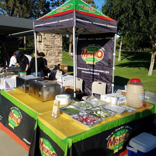 Little Mexico Chiquito catering tent with food warmers, serving dishes, and a beverage dispenser outdoors.