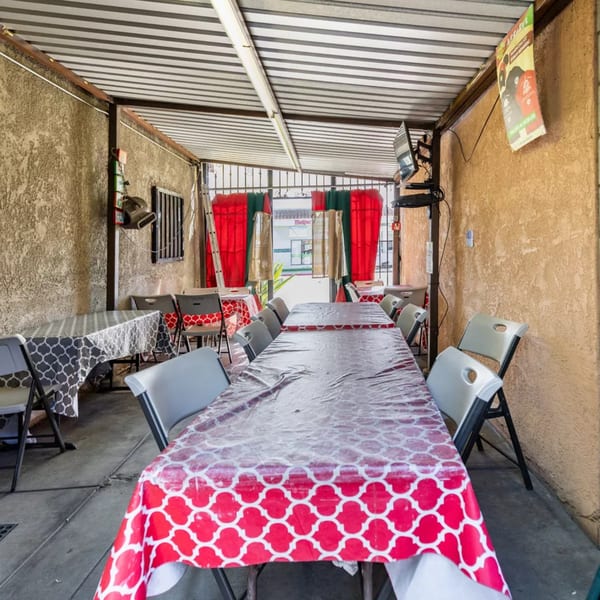 Outdoor patio dining area with long tables covered in red and white patterned tablecloths.